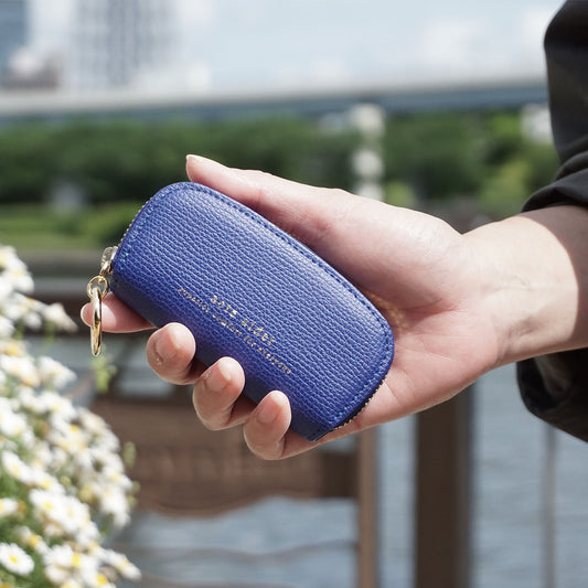 ラウンドファスナー小銭入れ エンボスレザー ブルー アークトエディー 片手で持った小銭入れを陽射しの下で見た様子