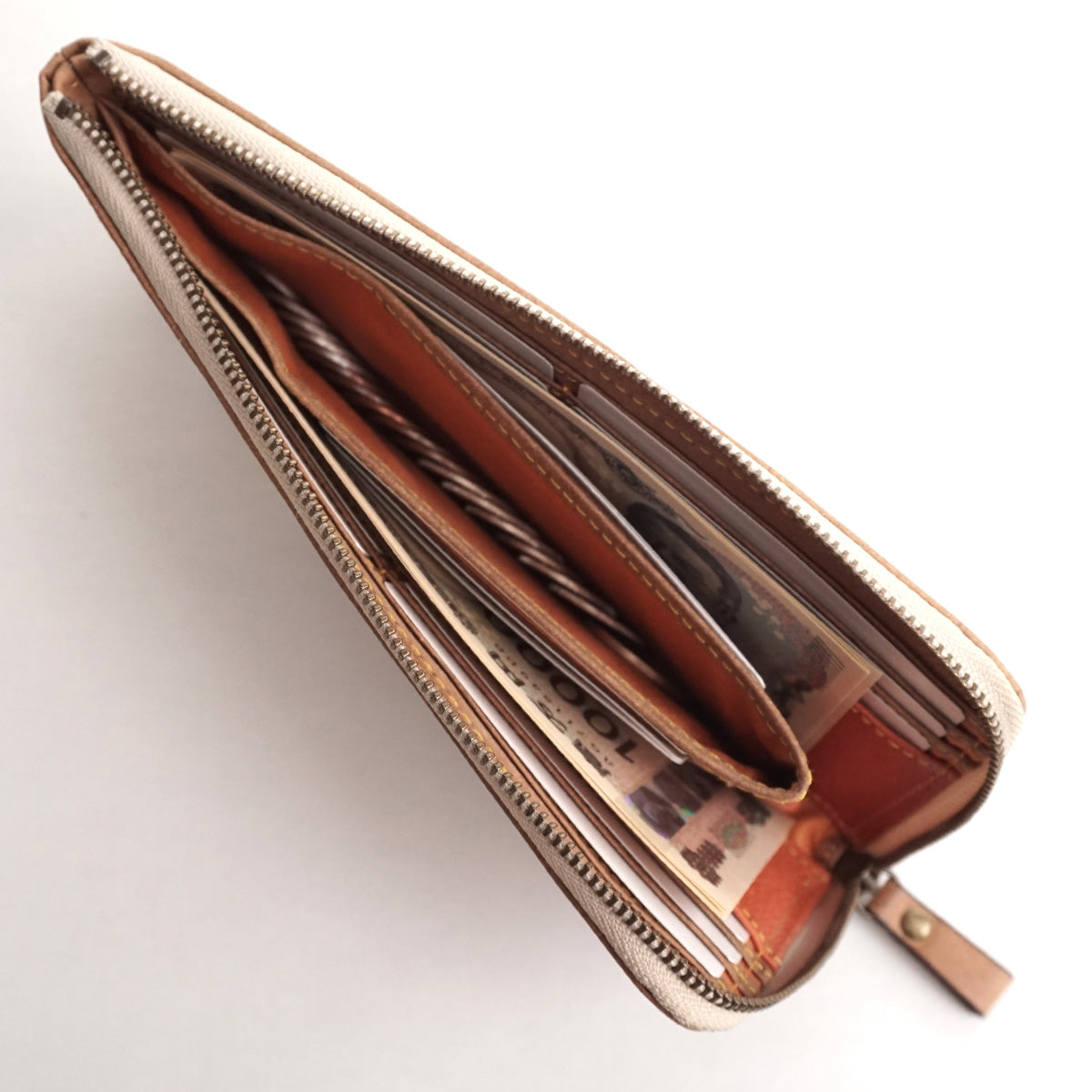 Lファスナー長財布　ジャーマンリサイクル　ベージュ　シャルム　駒屋　白いテーブルの上でファスナーを開けた長財布　中に紙幣、小銭、カードが入っている使用例を上から見た様子