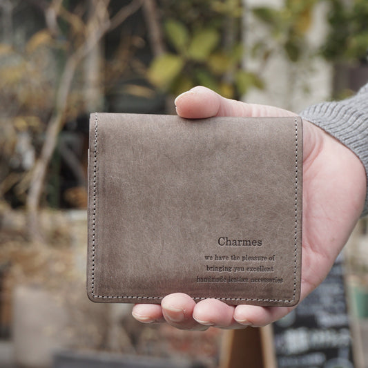 二つ折り財布　マルゴーシリーズ　クロ　シャルム　駒屋　カフェの前で右手に財布を持ちこちらに見せている様子　手元商品のアップ画像