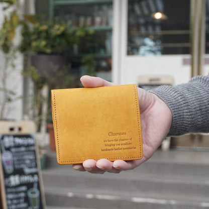 二つ折り財布　マルゴーシリーズ　イエロー　シャルム　駒屋　カフェの前で右手に財布を持ち、こちらに見せている様子