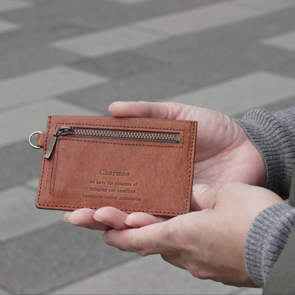 カードケース　マルゴーシリーズ　ブラウン　シャルム　駒屋　石畳に立つ女性が両手でカードケースを持ち、こちらに見せている様子　女性の手元のアップ画像