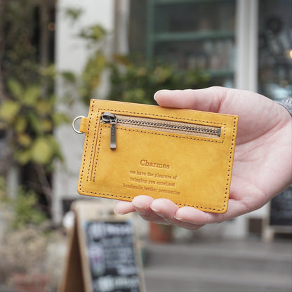 カードケース　マルゴーシリーズ　イエロー　シャルム　駒屋　日の当たるカフェの前で右手にカードケースを持ち、こちらに見せている手元のアップ画像